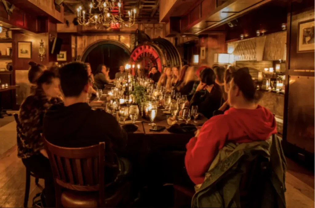 A photo of individuals around a dining table with a bank vault door in the background