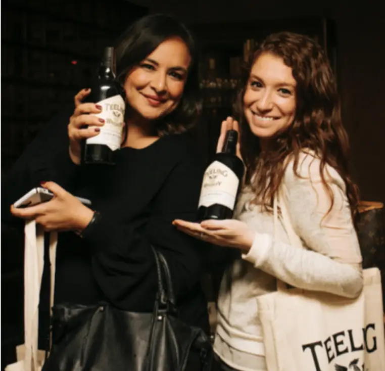 A photo of two female individuals holding Teeling Whiskey bottles